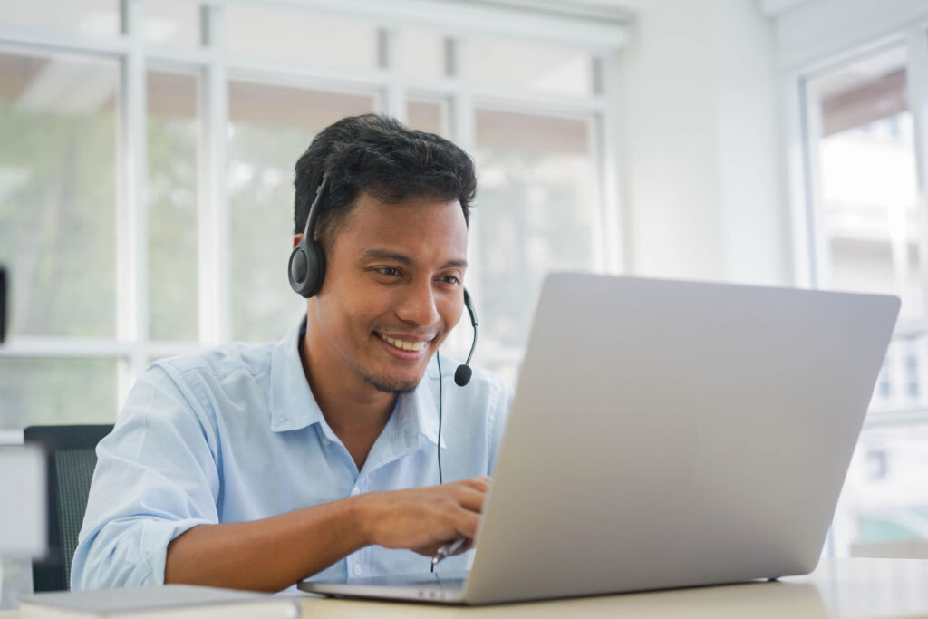 close up adult call center employee man smiling with wear headset while talking with customer in operation room office for contact us and telemarketing job concept