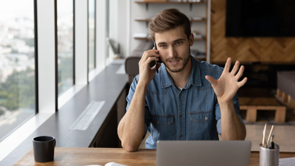 Young Caucasian businessman work on laptop talk on smartphone